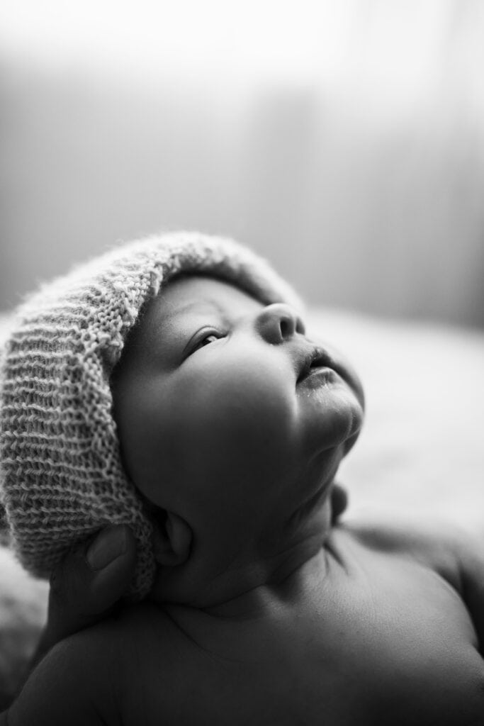 black and white image of a newborn baby with a white knit beanie cap.